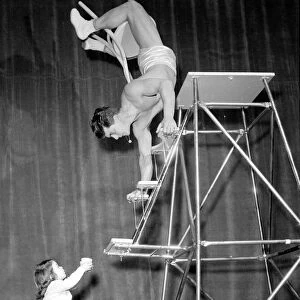 Children Acrobat. A young girl holding a cup looks up at a man walking down steps on his