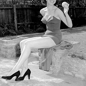 Woman wearing one piece swimsuit holding apple. Circa 1960