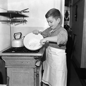 A young mixing ingredients together in a bowl in his kitchen at home. December 1952 C6055